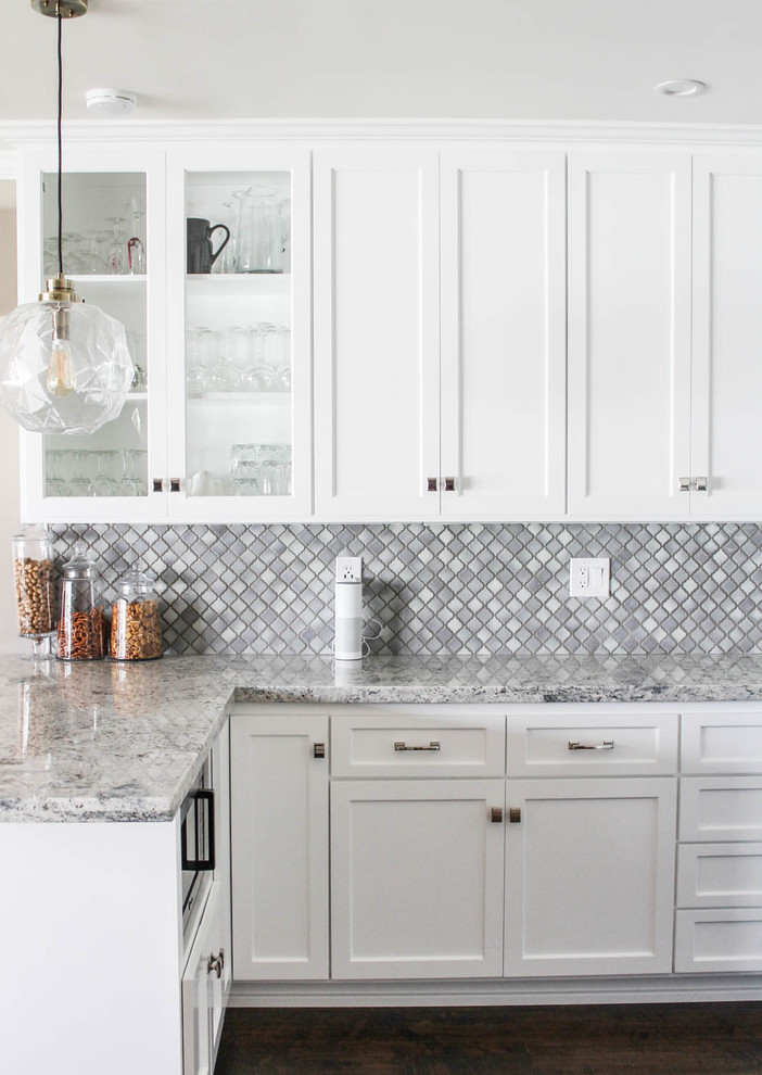 Small transitional l-shaped eat-in kitchen in Los Angeles with a single-bowl sink, shaker cabinets, granite benchtops, grey splashback, porcelain splashback, stainless steel appliances, with island, white cabinets and dark hardwood floors.