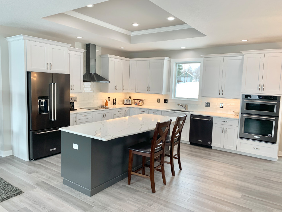 Design ideas for a large transitional l-shaped open plan kitchen in Other with an undermount sink, flat-panel cabinets, white cabinets, quartz benchtops, white splashback, glass tile splashback, black appliances, vinyl floors, with island, grey floor, white benchtop and recessed.