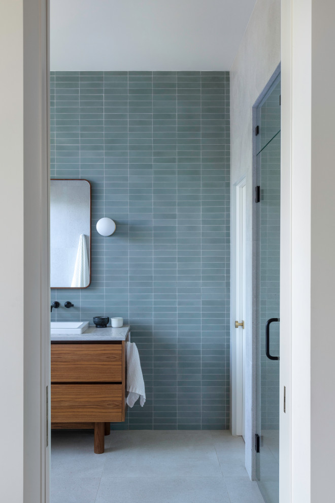 Photo of a midcentury master bathroom in Denver with flat-panel cabinets, medium wood cabinets, a freestanding tub, an alcove shower, blue tile, cement tile, porcelain floors, quartzite benchtops, a hinged shower door, white benchtops, an enclosed toilet, a double vanity, a built-in vanity and a drop-in sink.
