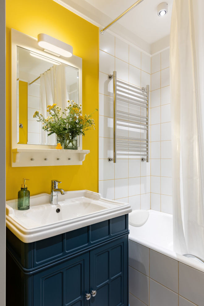 Bild på ett litet funkis vit vitt badrum, med luckor med profilerade fronter, blå skåp, ett undermonterat badkar, en dusch/badkar-kombination, vit kakel, keramikplattor, gula väggar, ett fristående handfat, bänkskiva i akrylsten, klinkergolv i keramik och svart golv