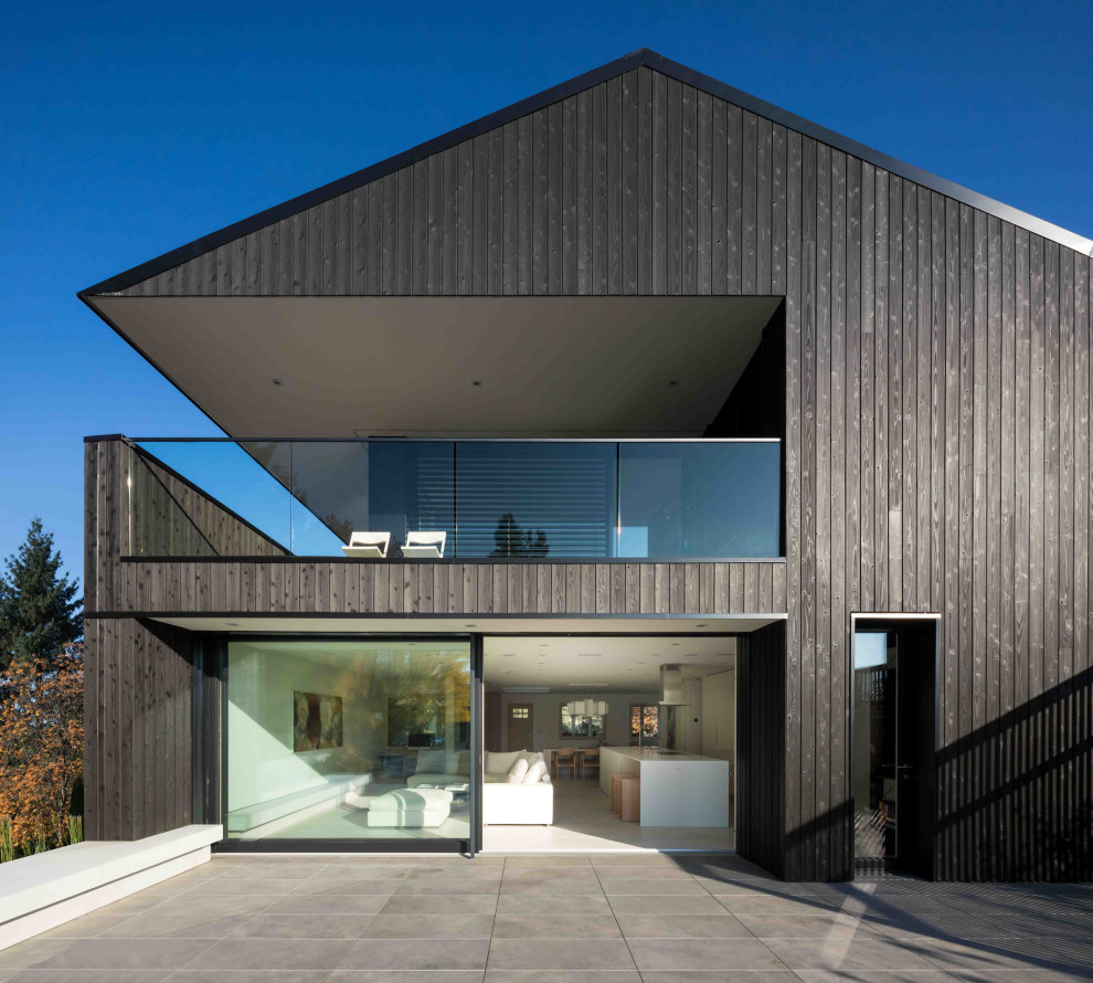Стильный дизайн: двухэтажный, деревянный, черный частный загородный дом среднего размера в стиле модернизм с металлической крышей и черной крышей - последний тренд