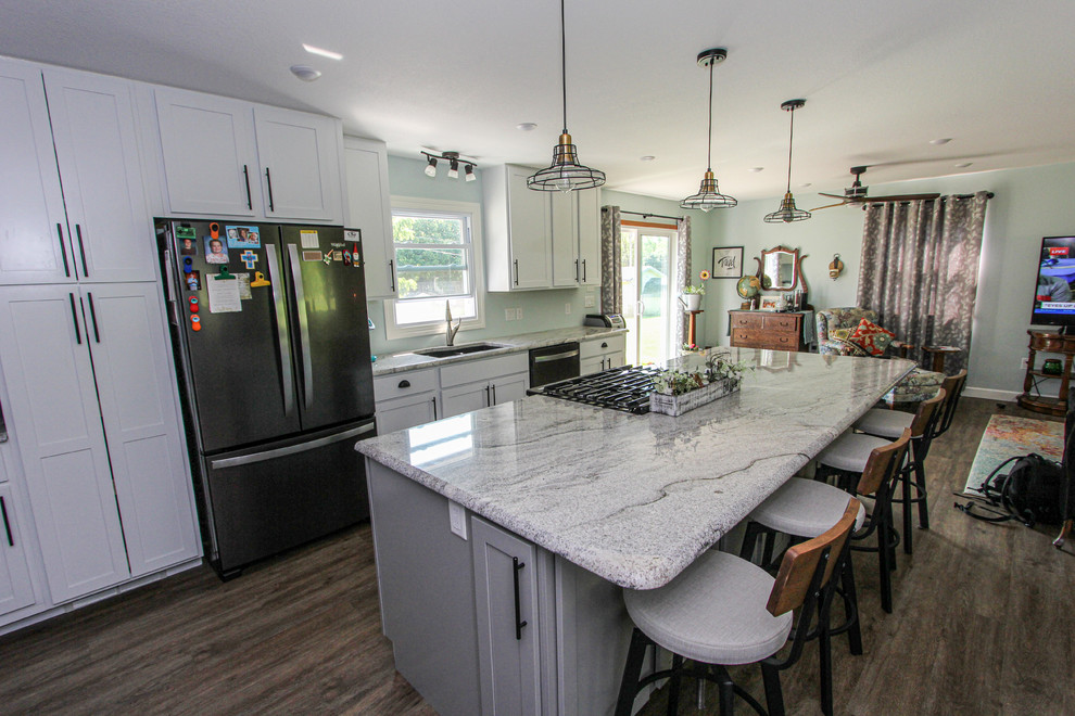 Example of a mid-sized transitional single-wall laminate floor and brown floor open concept kitchen design in Minneapolis with an undermount sink, shaker cabinets, gray cabinets, granite countertops, stainless steel appliances, an island and gray countertops