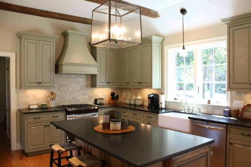 Design ideas for a mid-sized arts and crafts l-shaped separate kitchen in Boston with a farmhouse sink, raised-panel cabinets, green cabinets, solid surface benchtops, beige splashback, stone tile splashback, dark hardwood floors and with island.