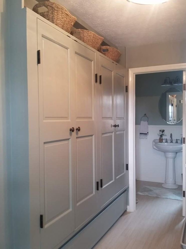 Photo of a mid-sized country l-shaped utility room in Indianapolis with raised-panel cabinets, soapstone benchtops, limestone floors, a stacked washer and dryer, beige floor and black benchtop.