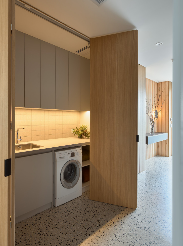 Mid-sized contemporary single-wall laundry room in Melbourne with an undermount sink, flat-panel cabinets, grey cabinets, solid surface benchtops, grey splashback, ceramic splashback, concrete floors, an integrated washer and dryer, multi-coloured floor and grey benchtop.