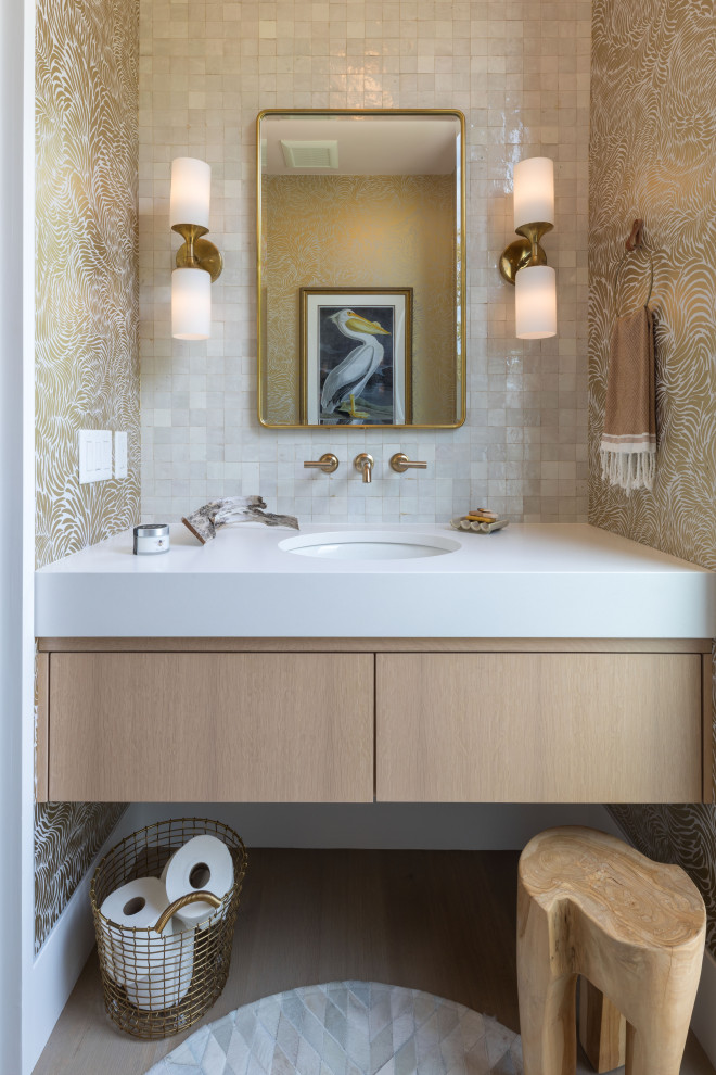 Example of a small trendy beige tile and glass tile light wood floor, gray floor and wallpaper powder room design in Boston with flat-panel cabinets, light wood cabinets, a wall-mount toilet, multicolored walls, an undermount sink, quartz countertops, white countertops and a floating vanity