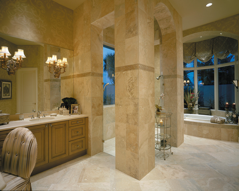 Inspiration for an expansive mediterranean master bathroom in Miami with an undermount sink, raised-panel cabinets, medium wood cabinets, solid surface benchtops, a drop-in tub, an open shower, a two-piece toilet, beige tile, stone tile, beige walls and travertine floors.