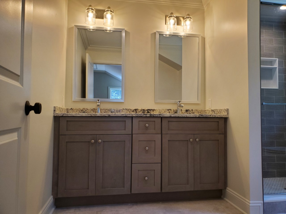 Photo of a large transitional master bathroom in New York with shaker cabinets, grey cabinets, an alcove shower, a two-piece toilet, gray tile, stone tile, white walls, porcelain floors, an undermount sink, granite benchtops, grey floor, a sliding shower screen, multi-coloured benchtops, a niche, a double vanity and a built-in vanity.
