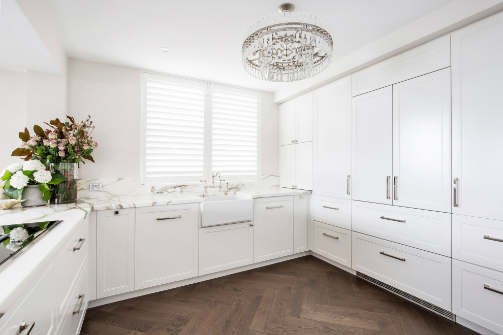 This is an example of a mid-sized transitional u-shaped open plan kitchen in Sydney with a farmhouse sink, recessed-panel cabinets, white cabinets, marble benchtops, multi-coloured splashback, marble splashback, black appliances, medium hardwood floors, with island, brown floor and multi-coloured benchtop.