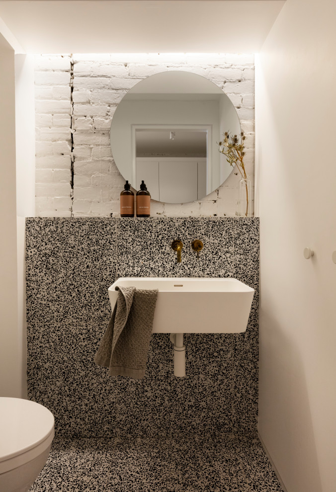Inspiration for a contemporary powder room in Montreal with black and white tile, ceramic tile, white walls, a wall-mount sink, multi-coloured floor and brick walls.