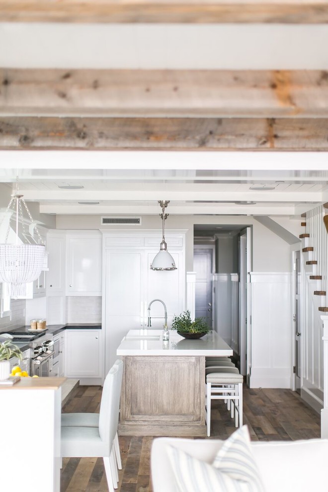Design ideas for a mid-sized beach style l-shaped open plan kitchen in Orange County with a farmhouse sink, shaker cabinets, white cabinets, quartz benchtops, white splashback, subway tile splashback, panelled appliances, dark hardwood floors, with island and brown floor.