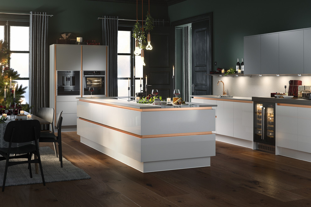 Large modern l-shaped open plan kitchen with an integrated sink, shaker cabinets, white cabinets, granite worktops, white splashback, marble splashback, black appliances, dark hardwood flooring, an island and brown floors.