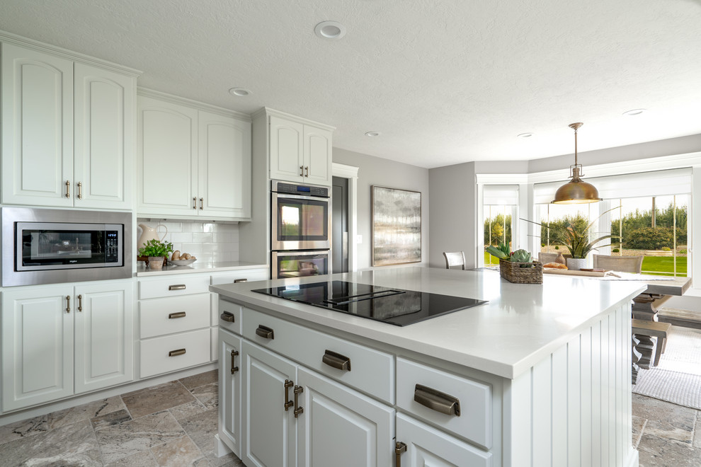 Transitional u-shaped travertine floor and brown floor open concept kitchen photo in Seattle with an undermount sink, raised-panel cabinets, white cabinets, quartz countertops, white backsplash, porcelain backsplash, stainless steel appliances, an island and white countertops