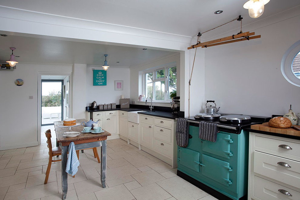 Design ideas for a small beach style galley open plan kitchen in Cornwall with a farmhouse sink, flat-panel cabinets, white cabinets, solid surface benchtops, black splashback, ceramic splashback, coloured appliances, ceramic floors and no island.