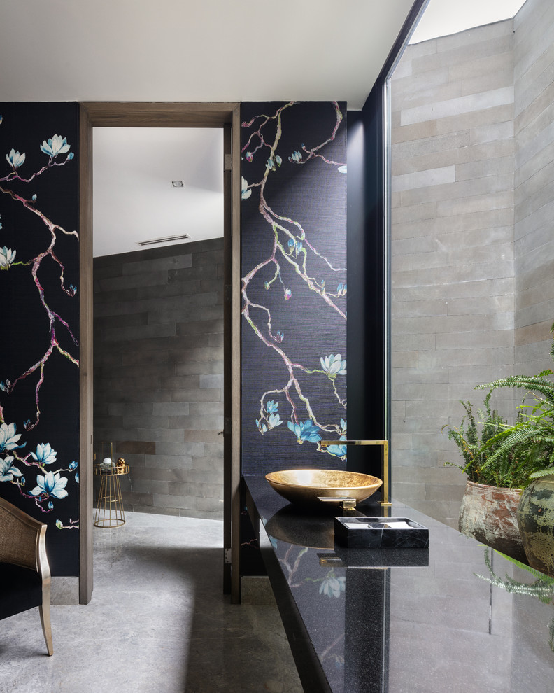 This is an example of a contemporary powder room with multi-coloured walls, a vessel sink, grey floor and black benchtops.