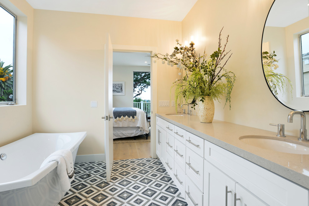 Photo of a mid-sized beach style master bathroom in Orange County with shaker cabinets, white cabinets, a freestanding tub, a corner shower, a two-piece toilet, white tile, beige walls, cement tiles, an undermount sink, concrete benchtops, multi-coloured floor, a hinged shower door and grey benchtops.