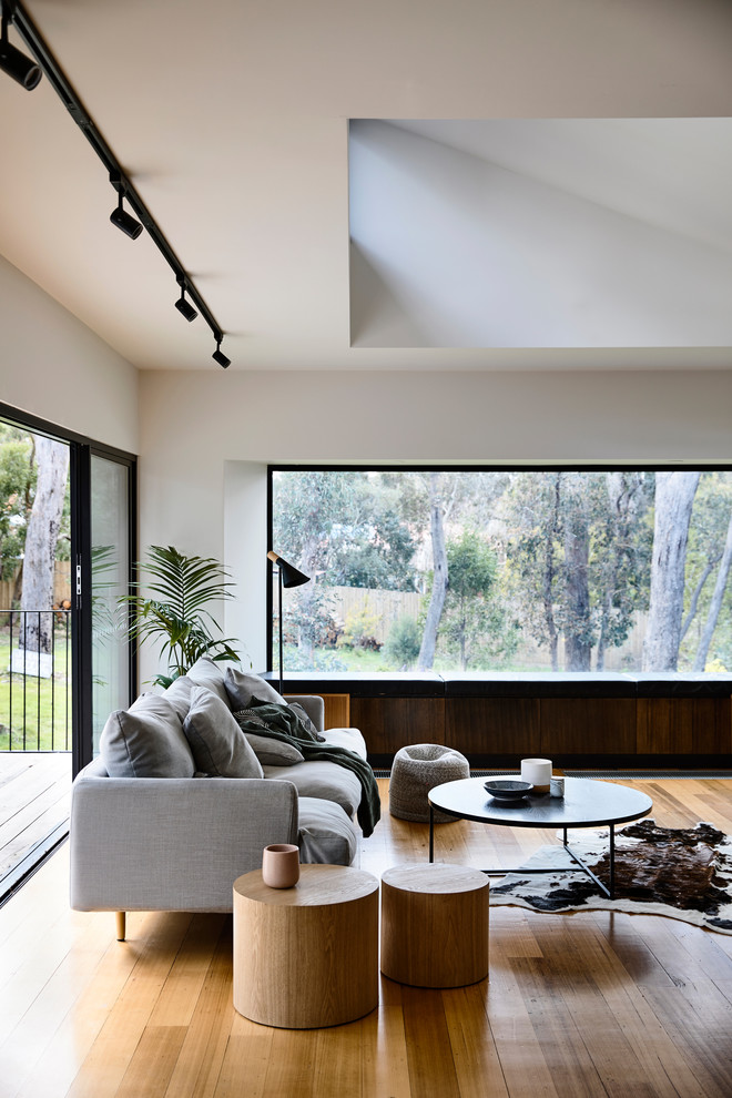Inspiration for a mid-sized contemporary open concept living room with white walls, light hardwood floors, a standard fireplace, a metal fireplace surround and a freestanding tv.