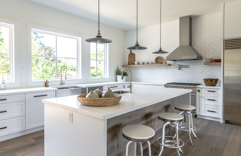 Example of a large transitional l-shaped medium tone wood floor open concept kitchen design in Toronto with a farmhouse sink, recessed-panel cabinets, white cabinets, white backsplash, subway tile backsplash, stainless steel appliances and an island