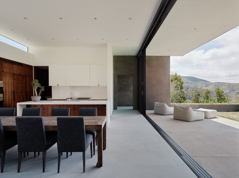 Inspiration for a modern l-shaped eat-in kitchen in Los Angeles with an undermount sink, flat-panel cabinets, white cabinets, white splashback, panelled appliances, concrete floors, with island, grey floor and white benchtop.