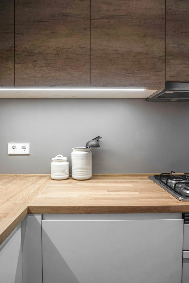 This is an example of a small scandinavian l-shaped open plan kitchen in Barcelona with a single-bowl sink, flat-panel cabinets, medium wood cabinets, wood benchtops, grey splashback, cement tile splashback, white appliances, concrete floors, no island, black floor and beige benchtop.