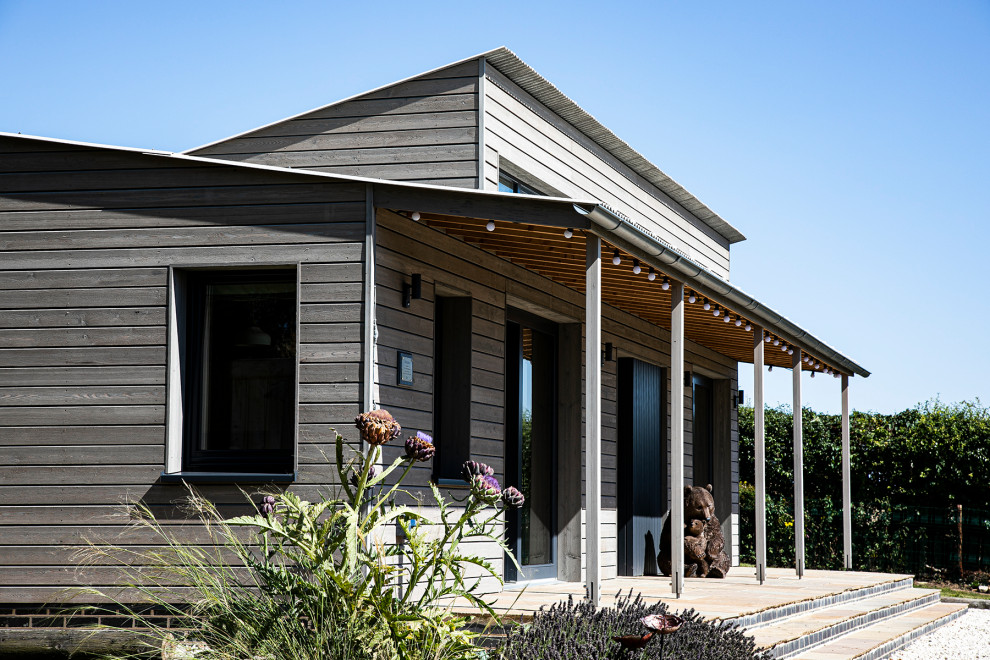 This is an example of a mid-sized contemporary one-storey brown exterior in Other with mixed siding, a gable roof, a mixed roof, a grey roof and board and batten siding.