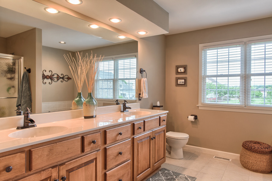 This is an example of a traditional master bathroom in Orange County with raised-panel cabinets, medium wood cabinets, beige walls, porcelain floors, an integrated sink and solid surface benchtops.