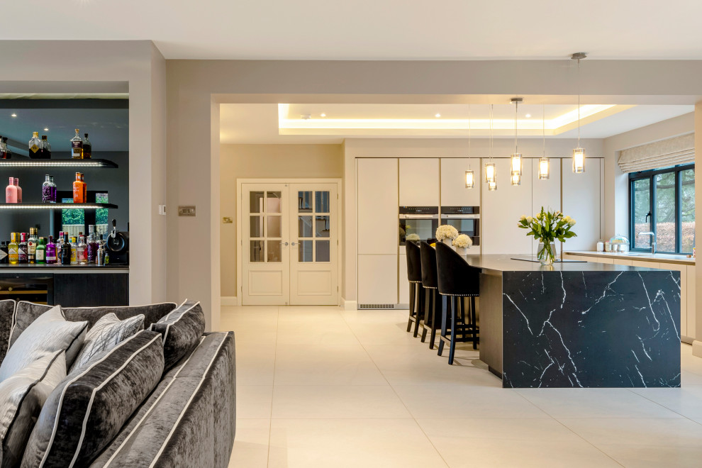 This is an example of a large contemporary l-shaped open plan kitchen in Cheshire with flat-panel cabinets, grey cabinets, tile benchtops, black appliances, porcelain floors, with island, grey floor, black benchtop and coffered.