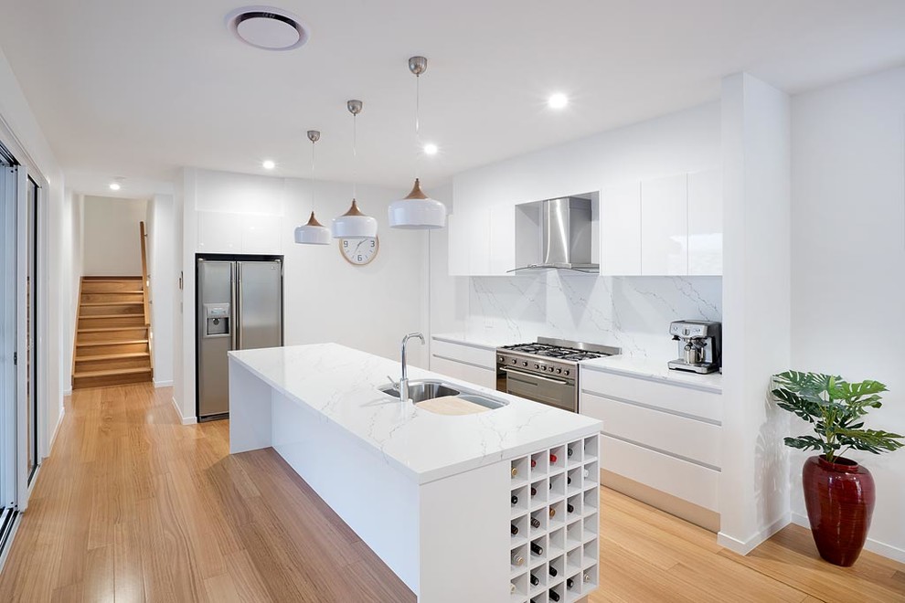 Design ideas for a small contemporary galley separate kitchen in Gold Coast - Tweed with stainless steel appliances, with island, flat-panel cabinets, white cabinets, white splashback, marble splashback, an undermount sink, quartz benchtops, light hardwood floors and beige floor.