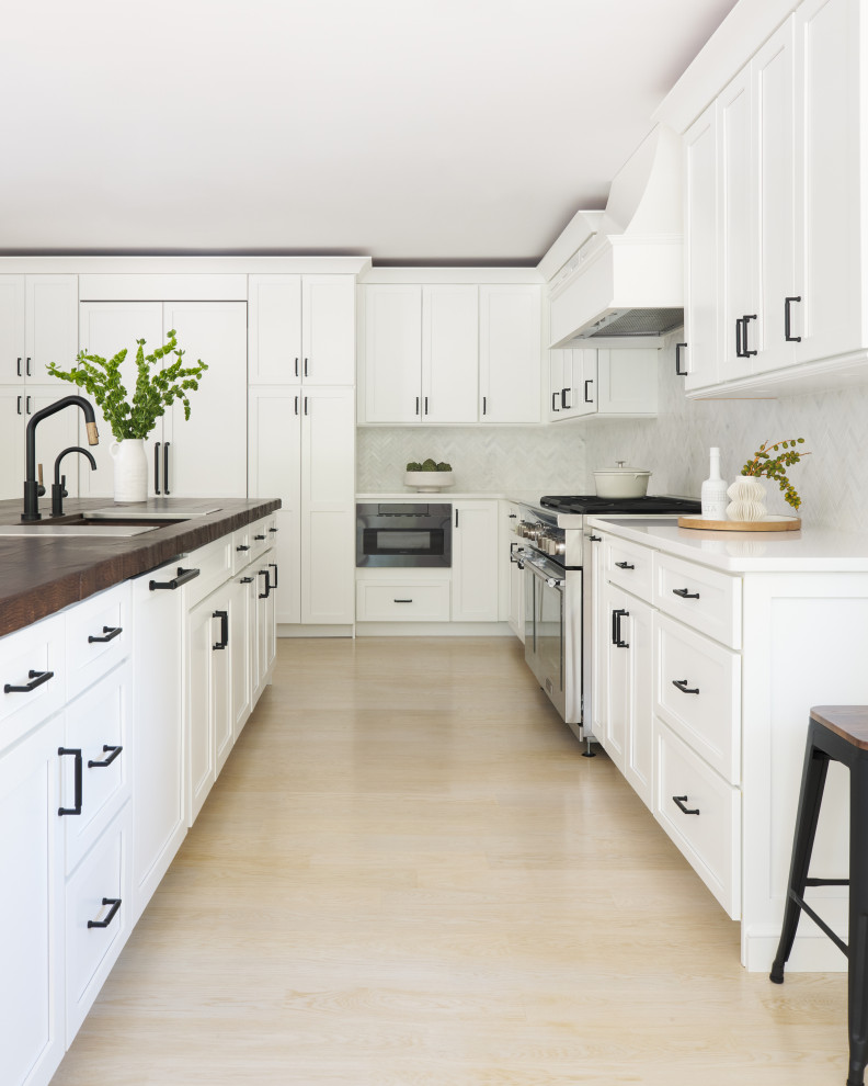 Large classic l-shaped kitchen/diner in New York with an integrated sink, recessed-panel cabinets, white cabinets, concrete worktops, white splashback, ceramic splashback, stainless steel appliances, light hardwood flooring, an island, white floors and multicoloured worktops.