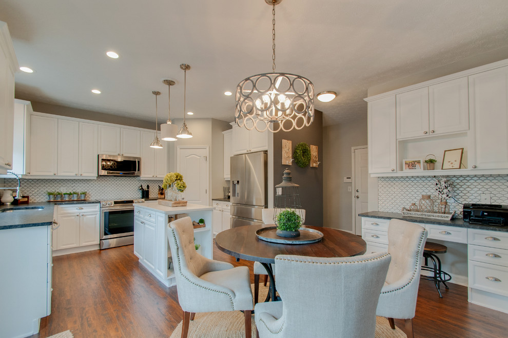 Photo of a mid-sized traditional u-shaped eat-in kitchen in Nashville with an undermount sink, recessed-panel cabinets, white cabinets, granite benchtops, white splashback, ceramic splashback, stainless steel appliances, medium hardwood floors, with island, brown floor and black benchtop.