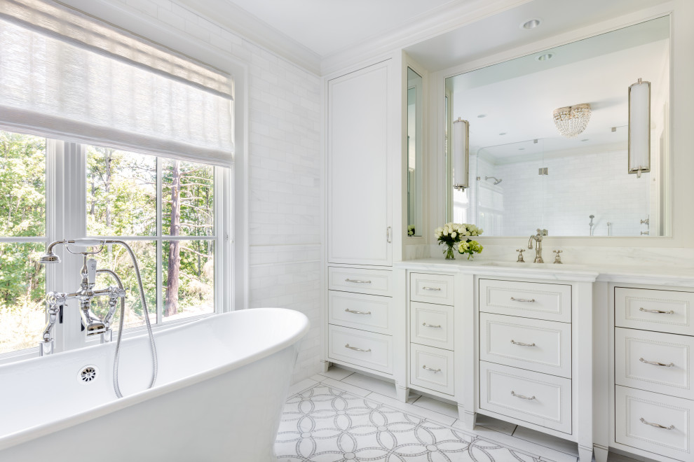 Inredning av ett klassiskt vit vitt badrum, med vita skåp, ett fristående badkar, en kantlös dusch, en bidé, marmorkakel, vita väggar, mosaikgolv, ett undermonterad handfat, marmorbänkskiva, vitt golv, dusch med gångjärnsdörr och luckor med infälld panel