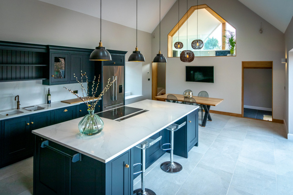 Small contemporary l-shaped kitchen/diner in Oxfordshire with a built-in sink, beaded cabinets, blue cabinets, marble worktops, grey splashback, granite splashback, ceramic flooring, an island, grey worktops, a vaulted ceiling, feature lighting, stainless steel appliances and grey floors.