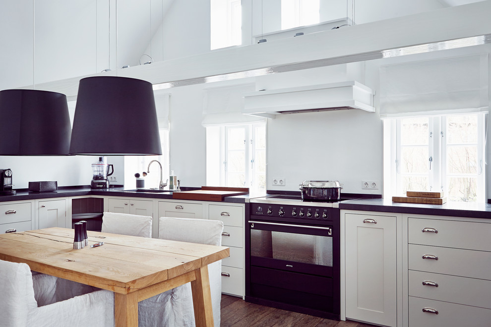 This is an example of a large country l-shaped separate kitchen in Hamburg with an undermount sink, white cabinets, medium hardwood floors, shaker cabinets, white splashback, black appliances and no island.