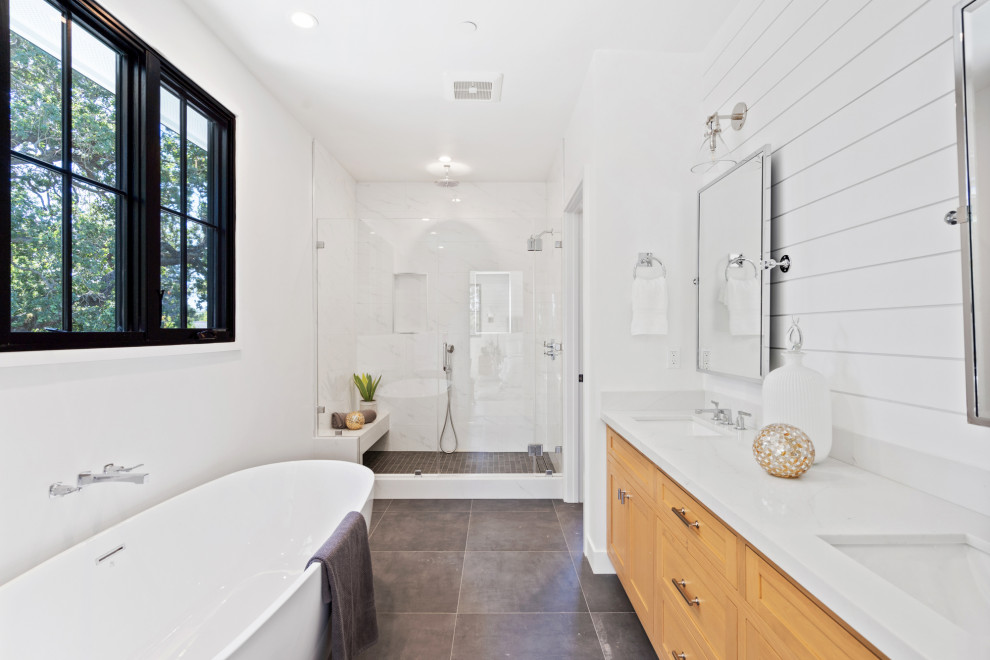 This is an example of a transitional master bathroom in San Francisco with shaker cabinets, medium wood cabinets, a freestanding tub, an alcove shower, white walls, an undermount sink, grey floor, a hinged shower door, white benchtops, a shower seat, a double vanity, a built-in vanity and planked wall panelling.