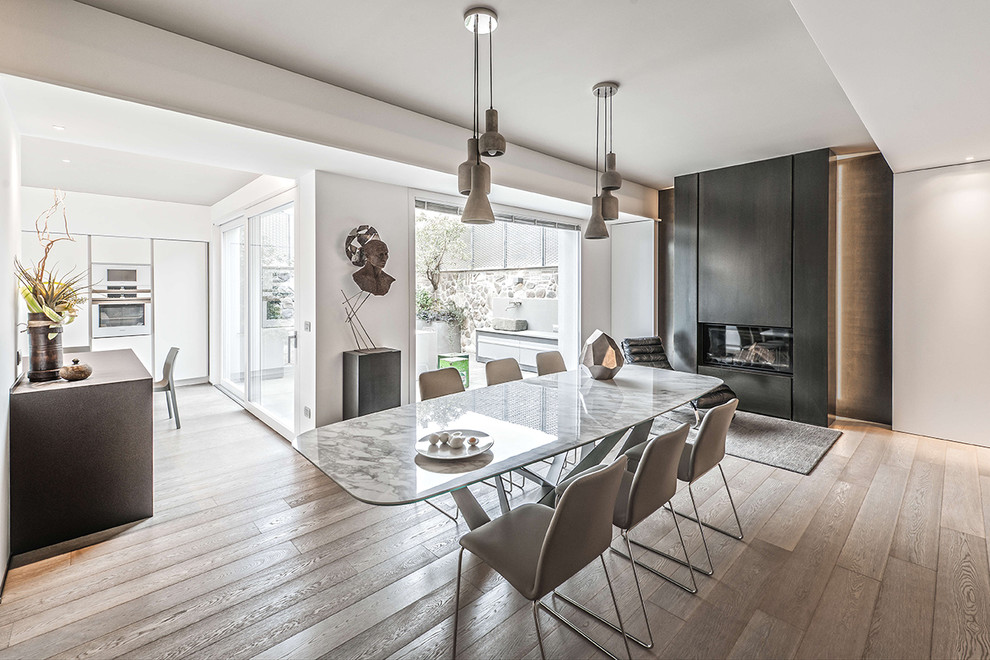 Photo of an expansive contemporary open plan dining in Milan with white walls, light hardwood floors, a ribbon fireplace and a metal fireplace surround.