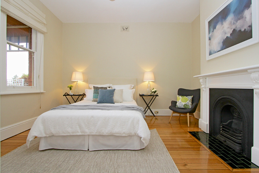 Inspiration for a transitional bedroom in Hobart with yellow walls, medium hardwood floors and a standard fireplace.