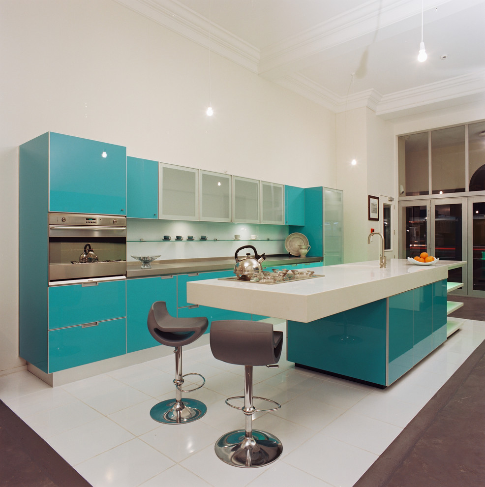 This is an example of a contemporary galley kitchen in Los Angeles with flat-panel cabinets, turquoise cabinets, solid surface benchtops and stainless steel appliances.