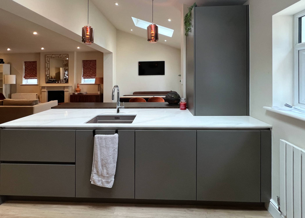 Photo of a medium sized contemporary grey and white l-shaped open plan kitchen in London with a single-bowl sink, flat-panel cabinets, grey cabinets, quartz worktops, white splashback, stainless steel appliances, an island, beige floors, white worktops, exposed beams and feature lighting.