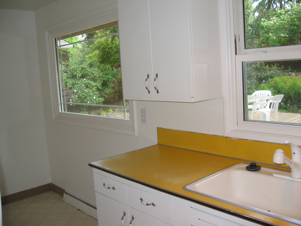 This is an example of a midcentury galley separate kitchen in Portland with a drop-in sink, flat-panel cabinets, beige cabinets, wood benchtops, beige splashback and white appliances.