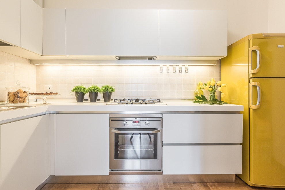 Design ideas for a mid-sized modern l-shaped kitchen in Bologna with flat-panel cabinets, white cabinets, solid surface benchtops, beige splashback, ceramic splashback, stainless steel appliances and medium hardwood floors.