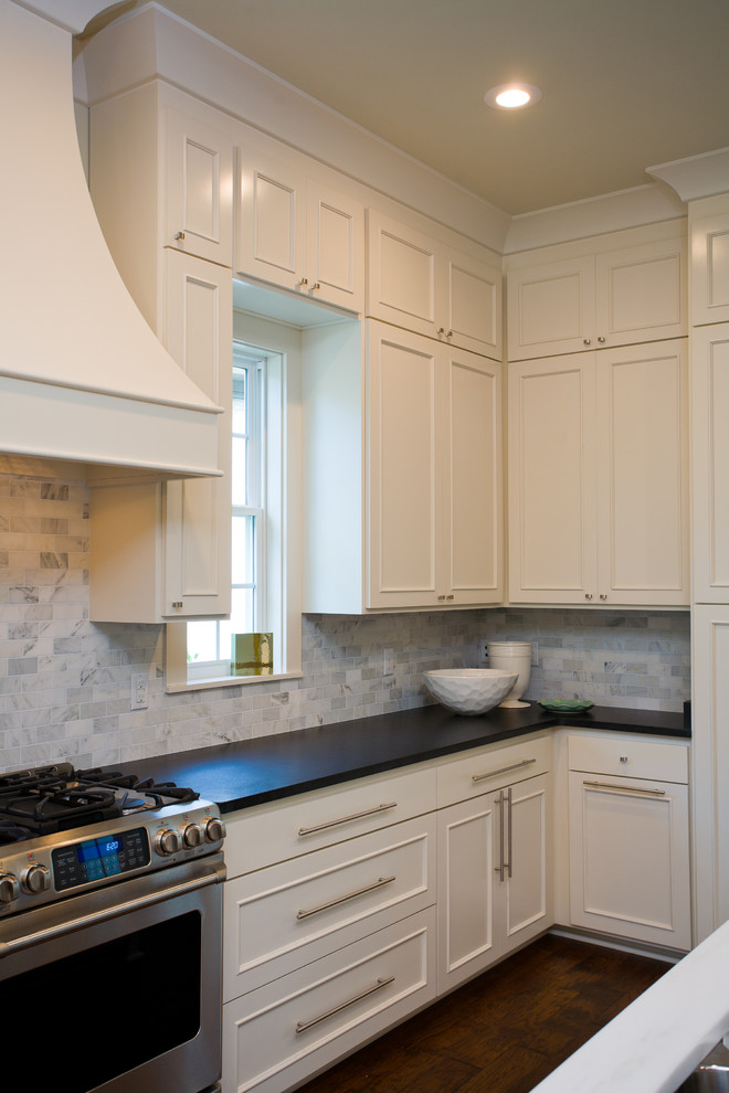 Traditional single-wall open plan kitchen in New Orleans with recessed-panel cabinets, white cabinets, white splashback, stone tile splashback, stainless steel appliances, dark hardwood floors and with island.