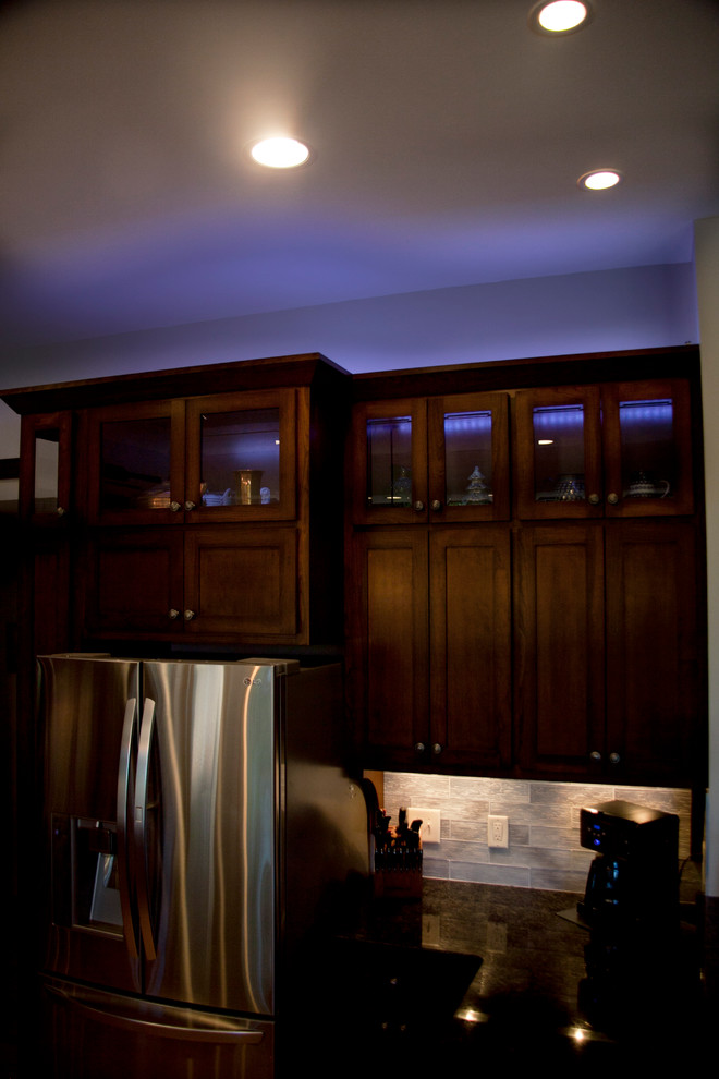 Inspiration for a transitional l-shaped light wood floor open concept kitchen remodel in Milwaukee with a farmhouse sink, shaker cabinets, medium tone wood cabinets, granite countertops, gray backsplash, glass tile backsplash, stainless steel appliances and an island
