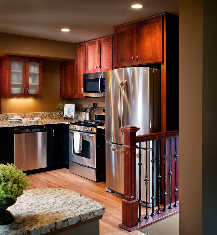 Eat-in kitchen - mid-sized craftsman l-shaped light wood floor eat-in kitchen idea in Omaha with shaker cabinets, black cabinets, granite countertops, beige backsplash, stone slab backsplash, stainless steel appliances, an island and an undermount sink