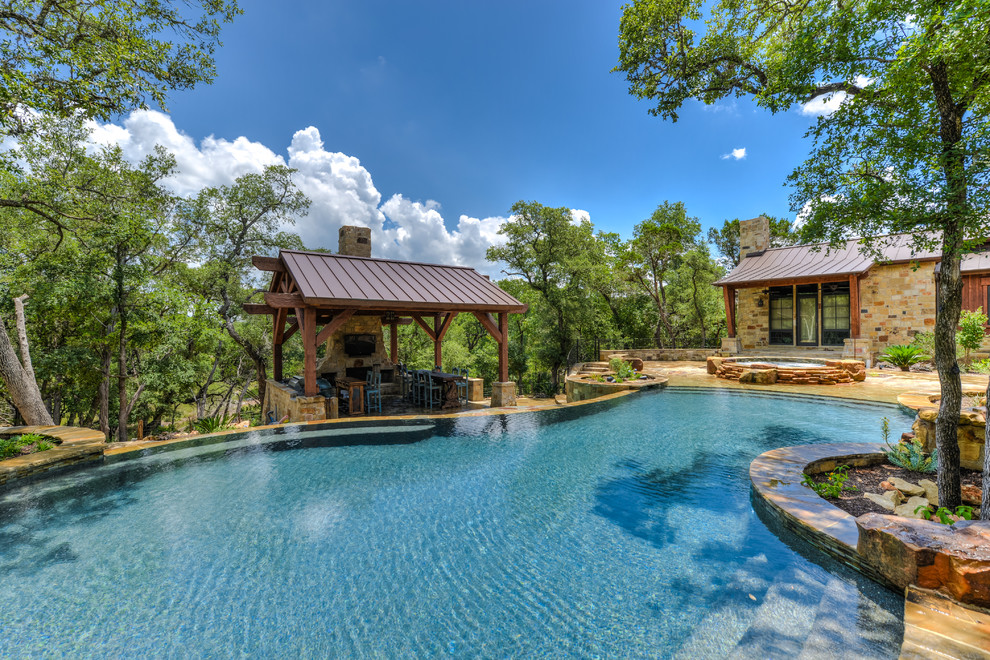 This is an example of a large country backyard custom-shaped infinity pool in Austin with a hot tub and natural stone pavers.