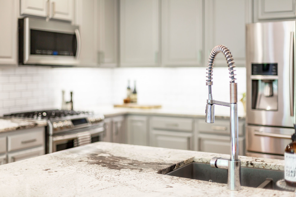 Example of a mid-sized transitional l-shaped medium tone wood floor eat-in kitchen design in Richmond with a farmhouse sink, gray cabinets, granite countertops, white backsplash, ceramic backsplash, stainless steel appliances, an island and white countertops