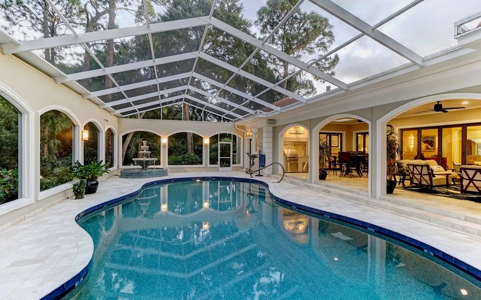 This is an example of a large traditional indoor custom-shaped lap pool in Tampa with a water feature and natural stone pavers.