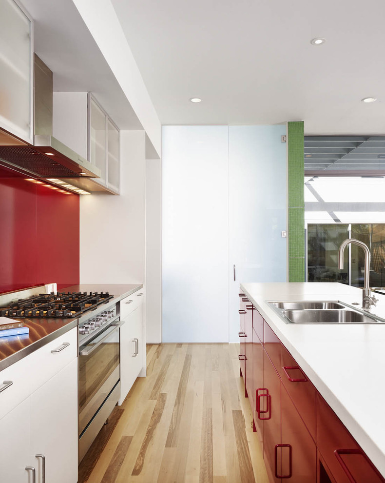 This is an example of a modern galley kitchen in Austin with a drop-in sink, flat-panel cabinets, red cabinets, concrete benchtops, red splashback, metal splashback and stainless steel appliances.