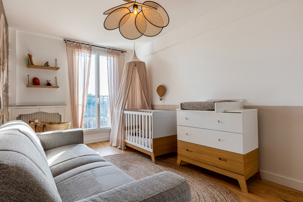 Diseño de habitación de bebé neutra vintage de tamaño medio con paredes beige, suelo de madera clara, suelo marrón y papel pintado