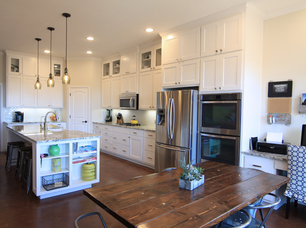 Photo of a large transitional l-shaped eat-in kitchen in Austin with a farmhouse sink, shaker cabinets, white cabinets, granite benchtops, white splashback, stainless steel appliances, concrete floors, with island and mosaic tile splashback.