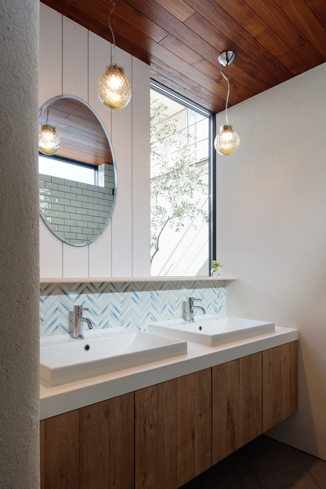 Inspiration for an asian bathroom in Other with flat-panel cabinets, medium wood cabinets, blue tile, white tile, mosaic tile, white walls, a vessel sink and white benchtops.